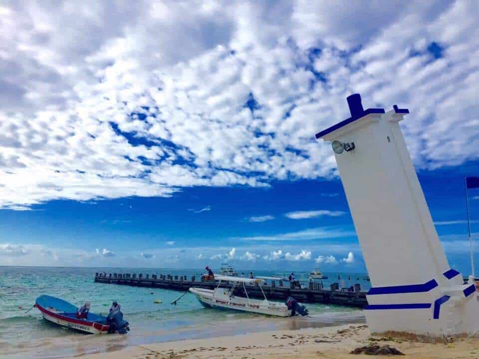 Leaning lighthouse beside boats and a pier in Puerto Morelos